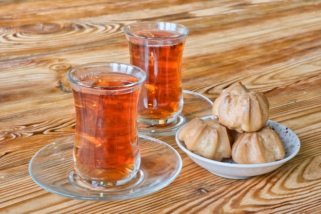 Twee traditionele Turkse glazen kopjes zwarte thee met zoete soesjes op houten tafel