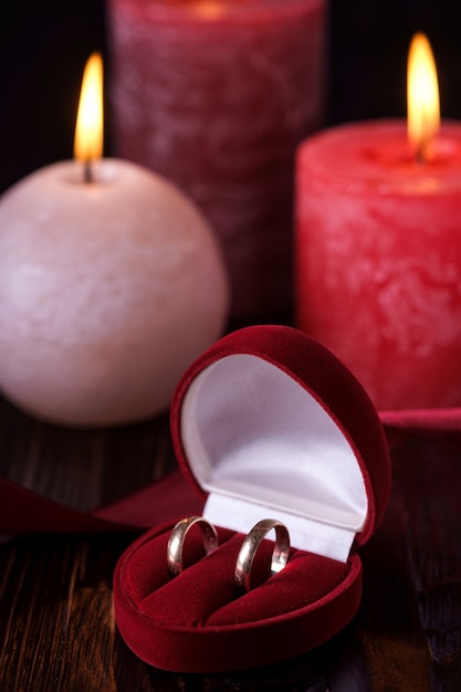 Twee trouwringen in rode geschenkdoos met drie wax vlam kaarslicht met lint in donker romantisch licht, liefde dating, Valentijnsdag, selectieve aandacht