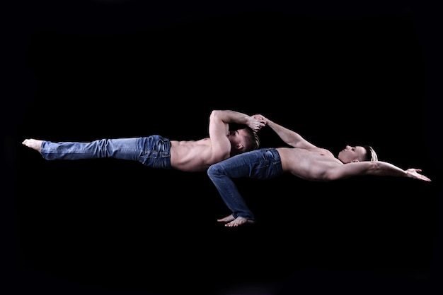 twee tweelingbroers in blauwe spijkerbroek met een naakte torso voeren acrobatische elementen uit, zwarte achtergrond