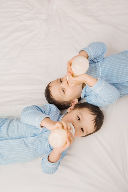 Twee tweelingjongens in pyjama's liggen op het bed met consumptiemelk uit flessen. uitzicht van boven. concept van huwelijk en vriendschap. concept van babyvoeding. ruimte voor tekst