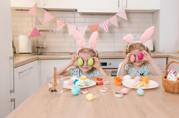 Twee tweelingmeisjes bereiden zich voor op de paasvakantie, spelen met paaseieren en houden ze vrolijk glimlachend in de buurt van hun ogen