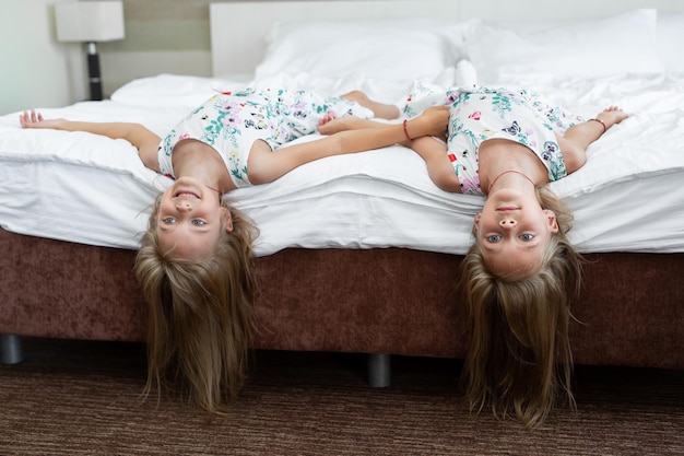 Twee tweelingzussen liggen ondersteboven op het bed.