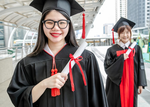 Twee universiteitsstudenten, aziatische vrouw draagt toga's en houdt diploma's