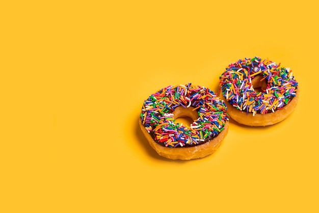 Twee van chocolade frosted donuts met hagelslag op gele achtergrond.