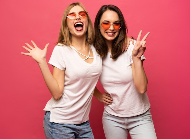 Twee verlaten vrouw die pret heeft en handen opheft. Staande op roze achtergrond. Geluksstemming.