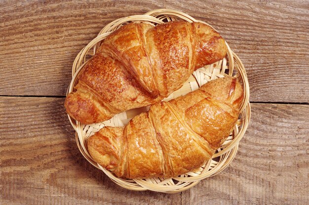 Twee verse croissants in rieten plaat op houten ondergrond, bovenaanzicht