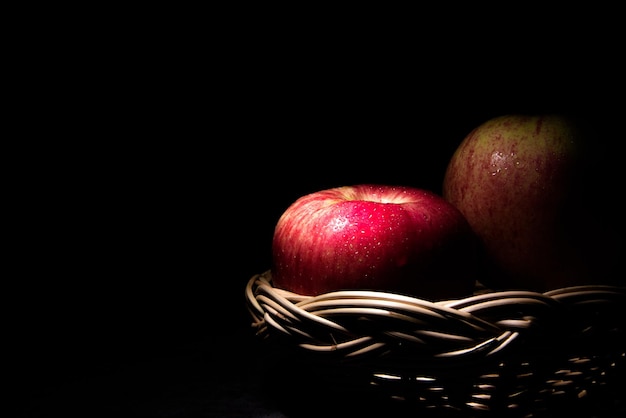 Twee verse rode appels in een mand Op een zwarte achtergrond met waterdruppeltjes vallen de lichten met ruimte voor tekst