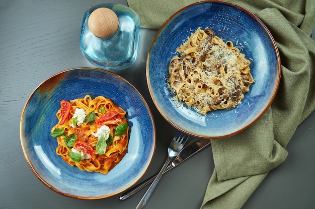 Twee verse, zelfgemaakte pasta met boschampignons en bolognese met tomaten in een blauwe kom op een houten tafel. Bovenaanzicht, plat lag
