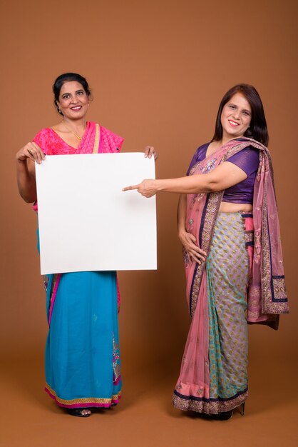 twee volwassen Indiase vrouwen die Sari Indiase traditionele kleding dragen samen met een wit bord