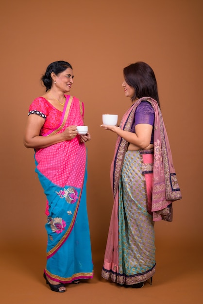 twee volwassen Indiase vrouwen die traditionele Sari-kleding dragen die samen thee drinken