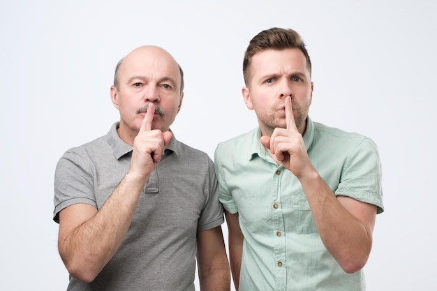 Foto twee volwassen mannen houden wijsvinger op lippen en proberen samenzwering te voorkomen