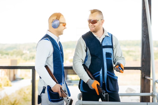 Twee volwassen mannen met een zonnebril en een geweervest oefenen met vuurwapenschieten