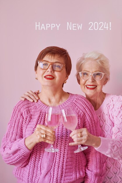 Foto twee volwassen vrouwen in roze truien drinken wijn en vieren.