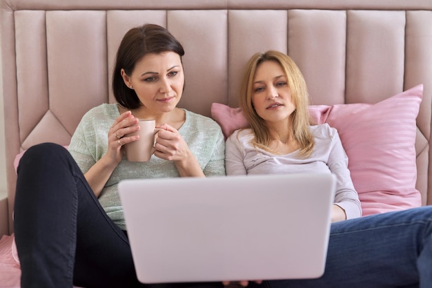 Twee volwassen vrouwen kijken naar laptop die thuis in bed zit