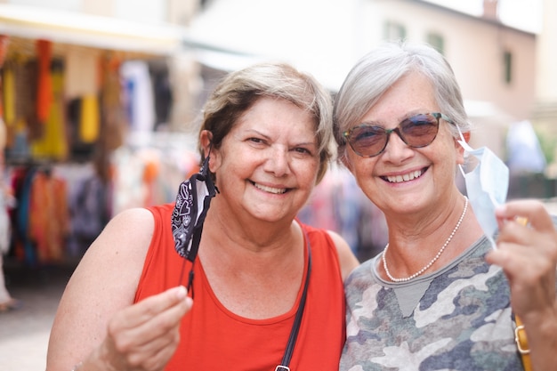 Twee volwassen vrouwen met een gelukkige uitdrukking, zetten de chirurgische maskers af die poseren voor een familieportret. Mensen, emoties en vriendschap