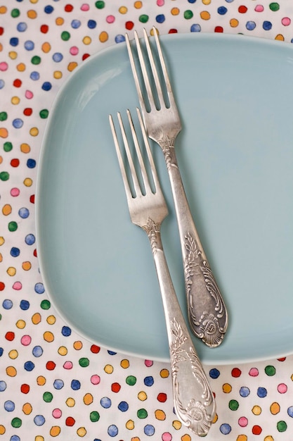 Twee vorken liggen op een tafelkleed naast een blauw bord.