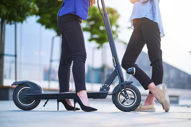 Twee vrienden chatten op straat op een zonnige dag. Een van hen rijdt op een elektrische scooter en draagt hakken.