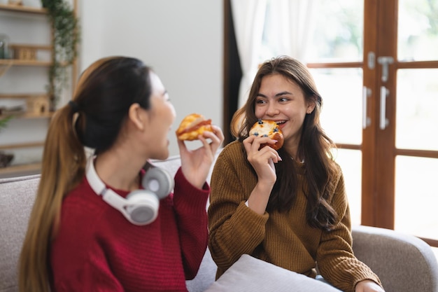 Twee vrienden genieten van het eten van croissants zittend op een bank in de woonkamer thuis