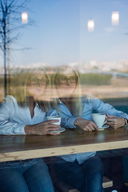 Twee vrienden genieten van koffie in een coffeeshop kijkend door een glas met reflecties zittend aan een tafel kletsend Bejaarde moeder en volwassen dochter in een café Moederdag Familiegelijkenis