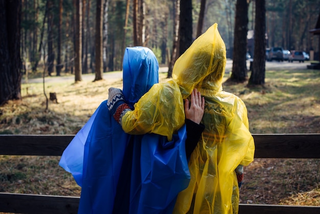 Twee vrienden in regenjassen met capuchon staan achter de camera op een toeristenparkeerplaats in het bos