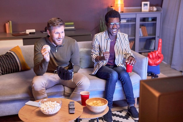 Twee vrienden kijken thuis naar sportwedstrijden en eten snacks verlicht door blauw licht