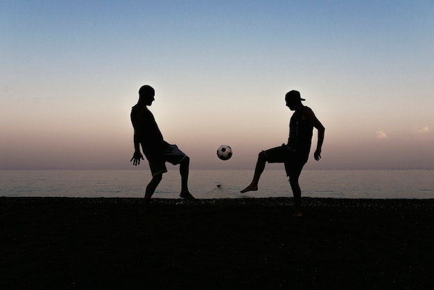 Twee vrienden voetballen op het strand.