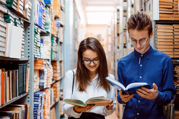 Twee vriendenstudenten die boeken lezen die zich in de lange gang in bibliotheek bevinden