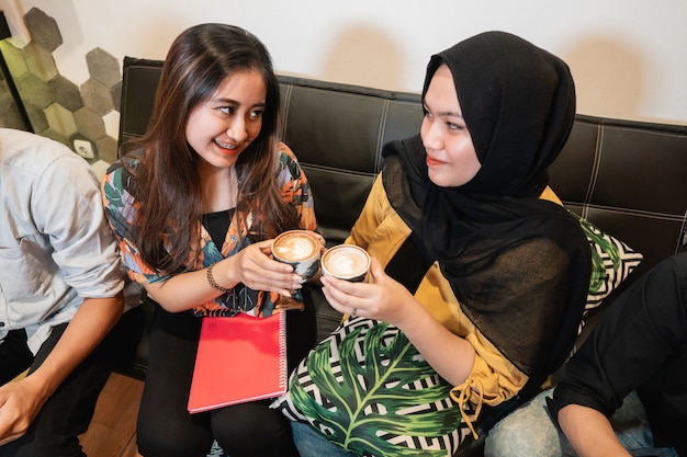 Twee vriendinnen houden een kopje koffie vast wanneer ze samen studeren in een coffeeshop