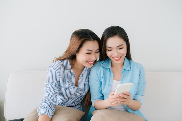 Twee vriendinnen kijken thuis naar de mobiele telefoon op de bank