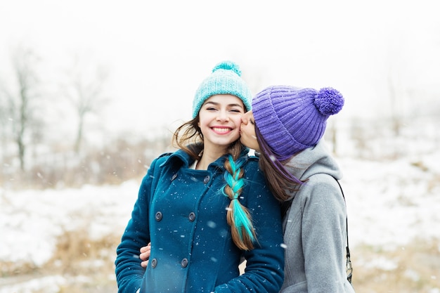 Twee vriendinnen knuffelen en zoenen buiten op besneeuwde winterdag