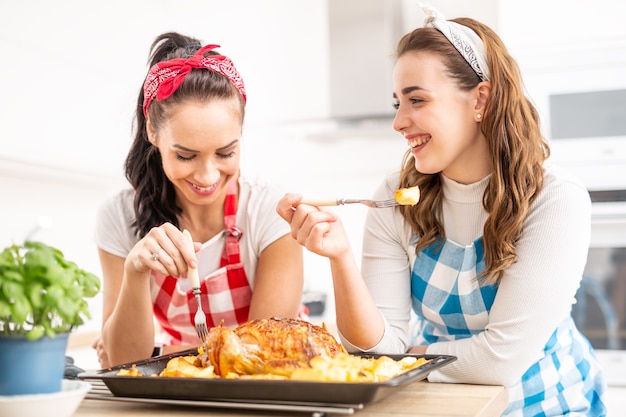 Twee vriendinnen lachen en proeven aardappelen en kip rechtstreeks van een bakplaat.