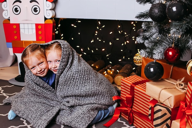 Twee vriendinnen of zussen omhelsd onder een deken lachend onder een kerstboom