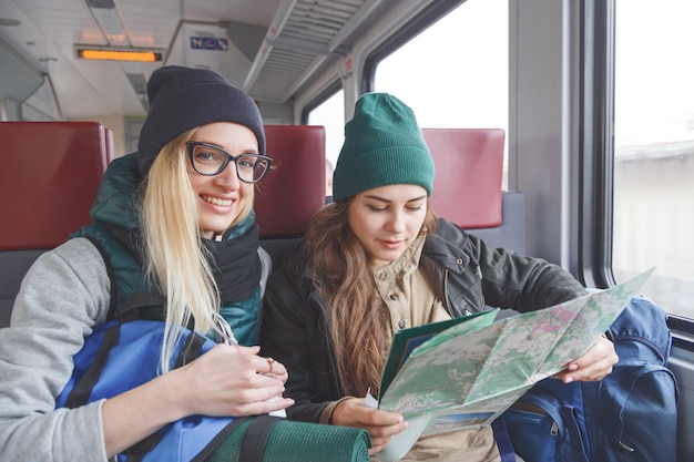 Twee vriendinnen reizigers met rugzakken en inventaris gaan de trein in en bekijken de verdere route op de kaart