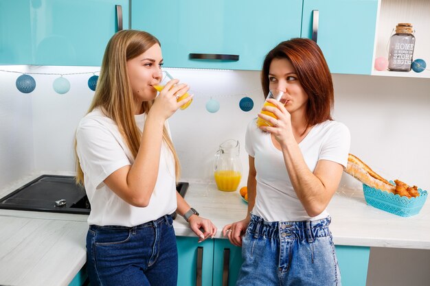 Twee vriendinnen staan in de keuken en drinken sinaasappelsap. vriendinnen chatten en delen geheimen in de keuken, ontbijt