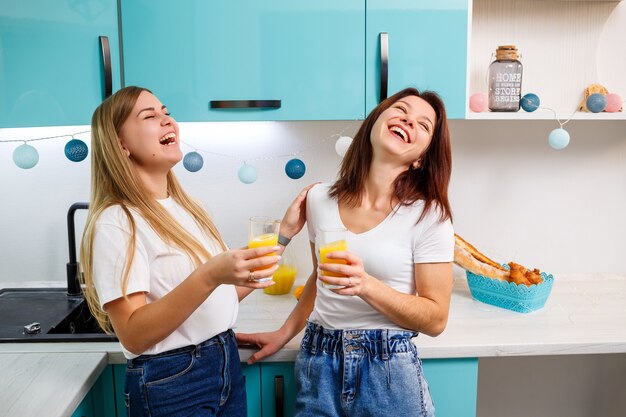 Twee vriendinnen staan in de keuken en drinken sinaasappelsap. Vriendinnen chatten en delen geheimen in de keuken, ontbijt