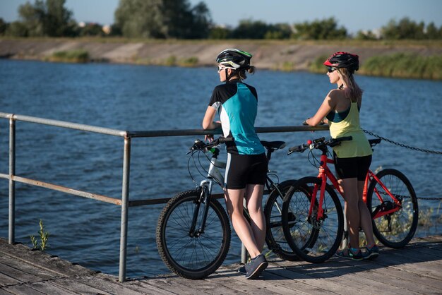 Twee vriendinnen vrouw met fietsen staan op de pierce en kijken naar het water