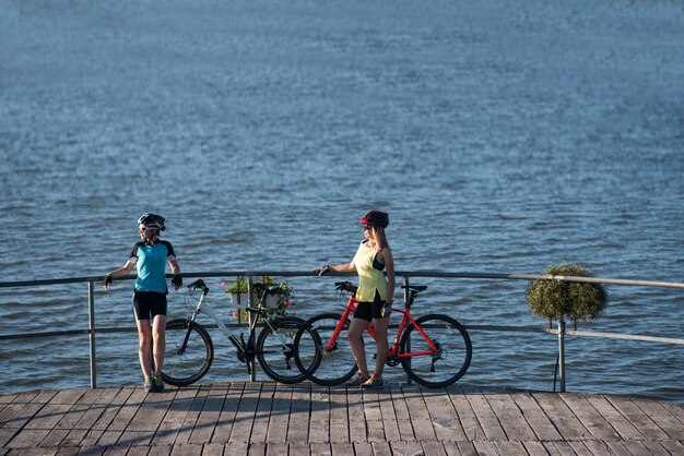 Twee vriendinnen vrouw met fietsen staan op de pierce en kijken naar het water