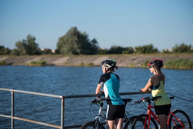 Twee vriendinnen vrouw met fietsen staan op de pierce en kijken naar het water