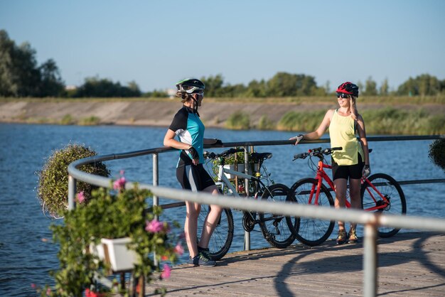 Twee vriendinnen vrouw met fietsen staan op de pierce en kijken naar het water