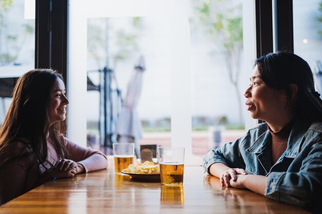 Twee vriendinnen zitten aan tafel in een bar terwijl ze met elkaar praten