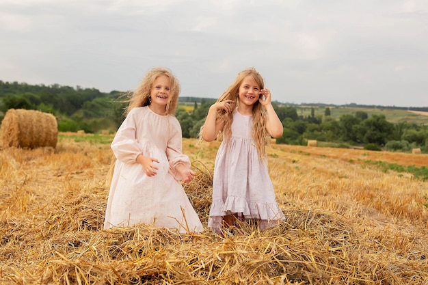 twee vrolijke blonde meisjes met lang haar in linnen jurken gooien hooi