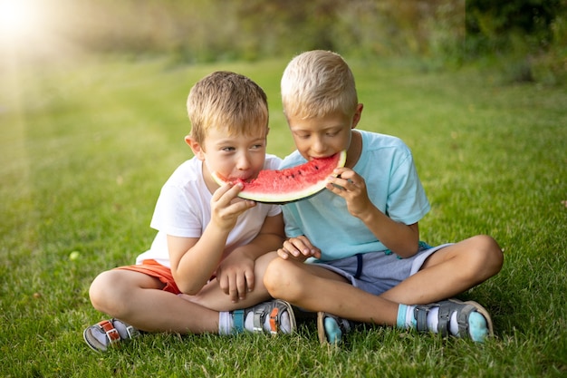 Twee vrolijke gelukkige jongenskinderen eten watermeloen in een groene open plek met zonnig gezond voedsel