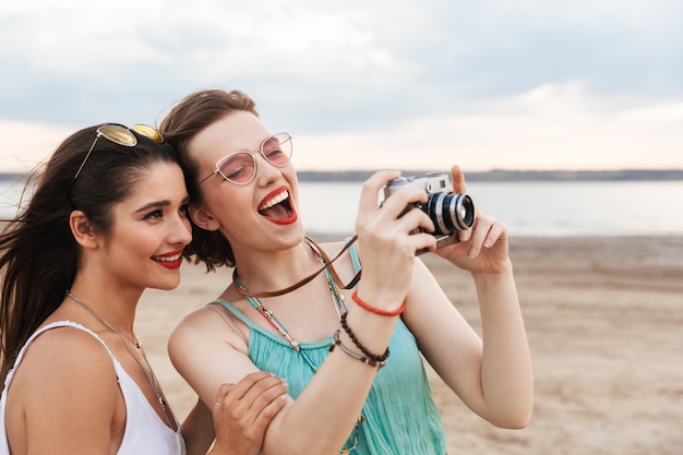 Twee vrolijke jonge meisjesvrienden die goede tijd op het strand doorbrengen, lachend