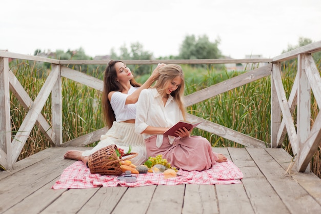 Twee vrolijke jonge vrouwen hebben een picknick buiten op een zomerse dag.