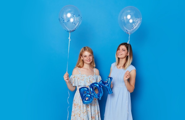 Twee vrolijke jonge vrouwen met blauwe ballonnen en ballon met de blauwe achtergrond van de inscriptiejongen