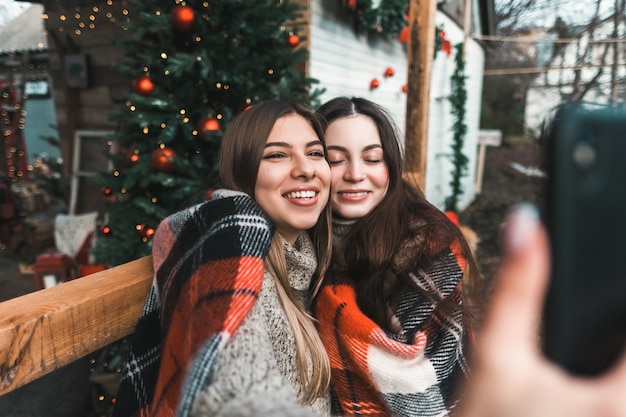 Twee vrolijke Kaukasische vrouwenvrienden die pret hebben en selfie maken op de achtertuin met kerstversiering.