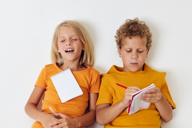 Foto twee vrolijke kinderen liggen op de grond met blocnotes en potloden onveranderde jeugdlevensstijl