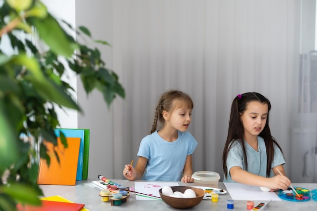 twee vrolijke, schattige meisjeszusjes schilderen paaseieren, oh lach, laat eieren zien en beschilderde handen