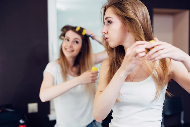 Twee vrolijke vriendinnen zetten hun haar thuis in krulspelden