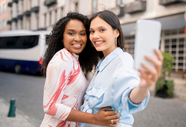 Twee vrolijke vrouwelijke vrienden met een smartphone nemen een selfie terwijl ze buiten lopen